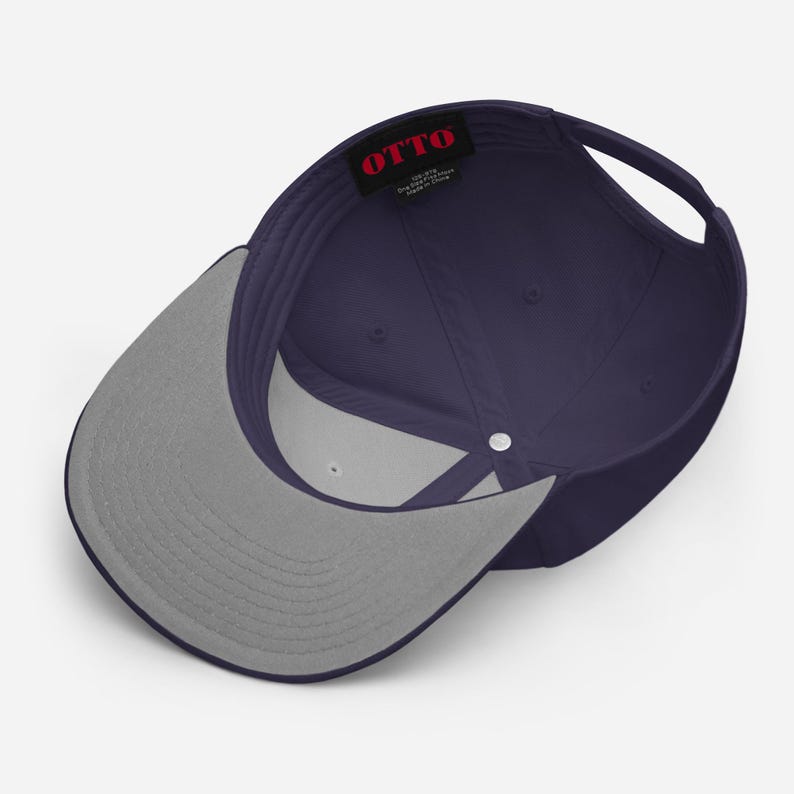 May include: A navy blue baseball cap viewed from the inside, featuring a grey underside of the brim and a black interior label with the red text OTTO. The cap has a structured crown with a central silver button and an adjustable back strap.