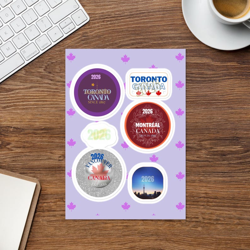 May include: A sticker sheet with a light purple background featuring small pink maple leaf icons. The sheet contains six circular and rectangular stickers with Canadian city themes, including Toronto, Montreal, and Vancouver, all displaying the year 2026.