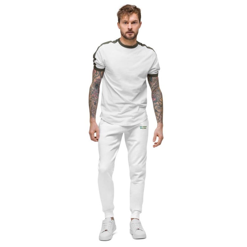 May include: A white t-shirt with dark green trim on the collar and sleeves, paired with matching white joggers. The joggers feature small green text on the upper thigh area. The outfit is completed with plain white trainers.