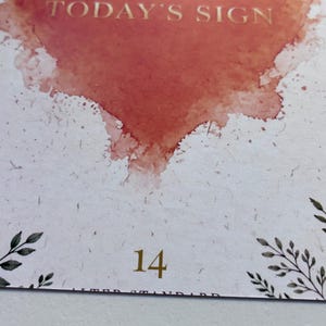 May include: A rectangular card with rounded corners featuring a watercolour-style orange heart at the top, the text TODAY'S SIGN in gold, and the number 14 in gold at the bottom. The card has a white speckled background with green botanical illustrations.