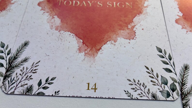 May include: A rectangular card with rounded corners featuring a watercolour-style orange heart at the top, the text TODAY'S SIGN in gold, and the number 14 in gold at the bottom. The card has a white speckled background with green botanical illustrations.