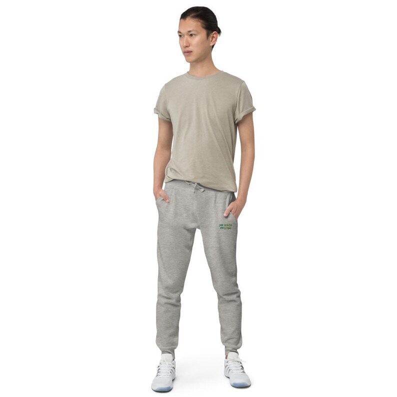 May include: A beige short-sleeved crew neck t-shirt and heather grey jogger sweatpants with a drawstring waist and ribbed cuffs. The sweatpants feature small green text on the upper left thigh area. The outfit is paired with white athletic trainers.