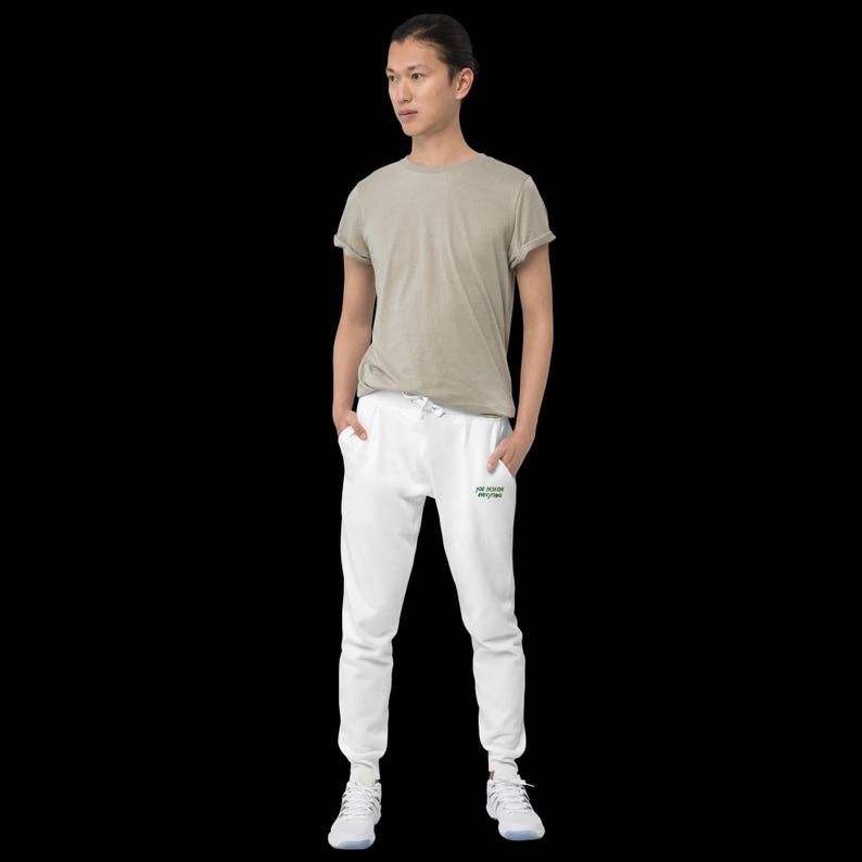 May include: A beige short-sleeved t-shirt and white joggers with a drawstring waist. The joggers feature small green and black text on the upper left thigh that reads "see soccer everyday". The outfit is completed with white athletic trainers.