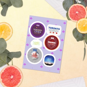 May include: A light purple sticker sheet featuring small maple leaf icons and six distinct stickers. The designs include text for Toronto, Montreal, and Vancouver, Canada, with the year 2026, alongside a skyline image and a plain 2026 label.