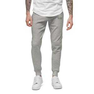 May include: Light grey sweatpants featuring a small green embroidered text on the upper right thigh that reads "you deserve everything". The sweatpants have a tapered leg design with ribbed cuffs at the ankles and a white t-shirt tucked in above.