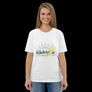 Pode incluir: Uma t-shirt branca de manga curta com uma impress&atilde;o gr&aacute;fica de uma paisagem florestal, um sol nascente, o texto COLLINGWOOD e as coordenadas 44.5000&deg;N. O design inclui pinheiros verdes, um toque de pincelada amarela e linhas pretas.