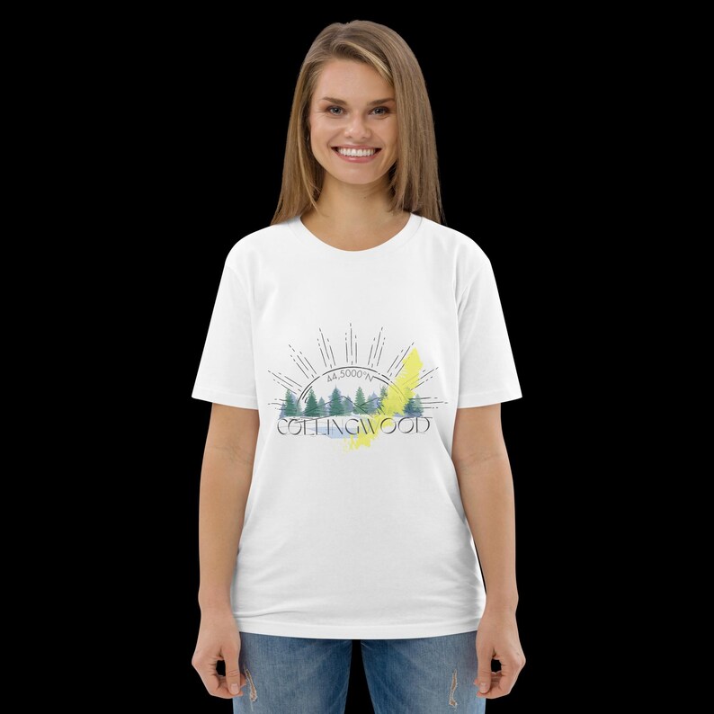 Pode incluir: Uma t-shirt branca de manga curta com uma impress&atilde;o gr&aacute;fica de uma paisagem florestal, um sol nascente, o texto COLLINGWOOD e as coordenadas 44.5000&deg;N. O design inclui pinheiros verdes, um toque de pincelada amarela e linhas pretas.