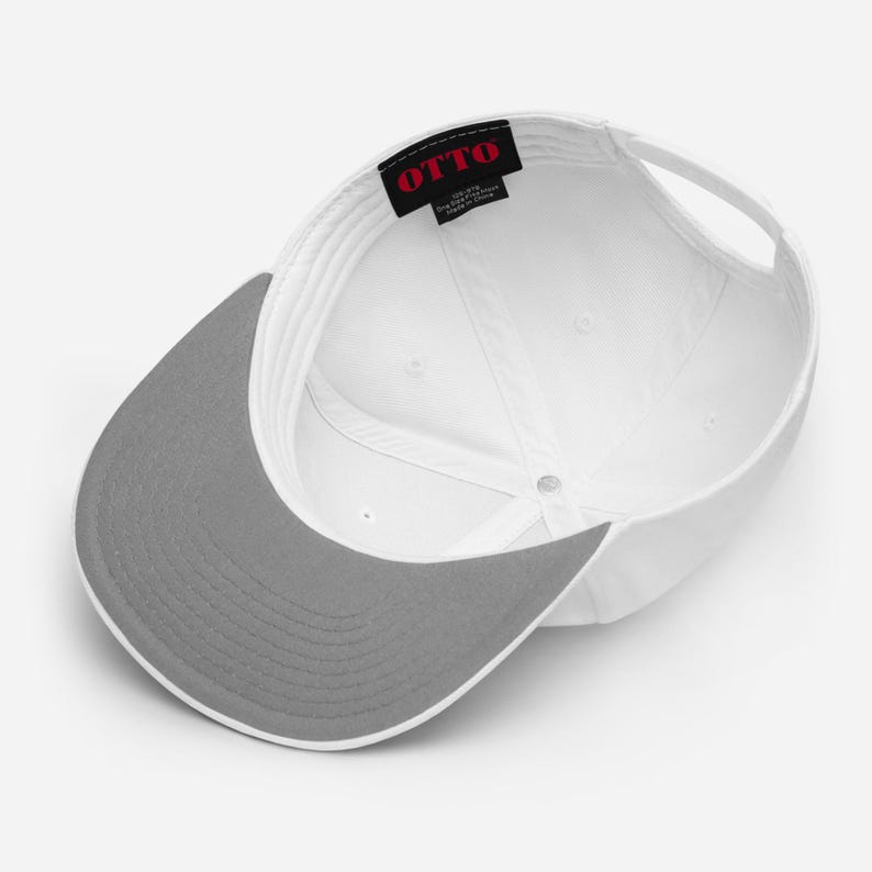 May include: A white baseball cap viewed from the inside, featuring a grey brim and a black interior label with the red text OTTO. The cap has a structured crown with white stitching and a white adjustable strap at the back for a secure fit.