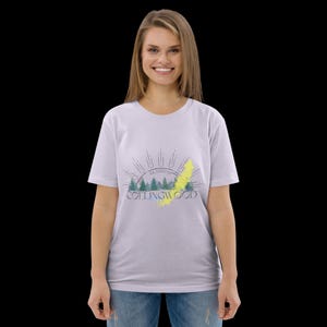 Pode incluir: Uma t-shirt de manga curta em roxo claro com uma impress&atilde;o gr&aacute;fica de pinheiros verdes, um raio amarelo e raios de sol. O texto "COLLINGWOOD" est&aacute; impresso em letras azul-escuras abaixo das &aacute;rvores com as coordenadas 44.5000&deg;N.
