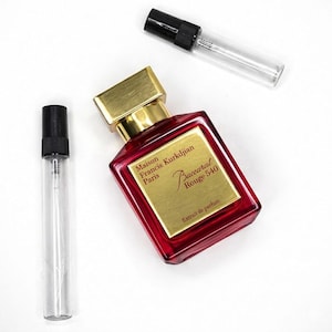 May include: A red perfume bottle with a gold cap and label, alongside two clear glass vials with black spray tops. The label reads "Maison Francis Kurkdjian Paris Baccarat Rouge 540 Extrait de parfum."
