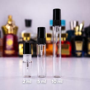 May include: Three clear glass perfume spray bottles with black caps, labelled 2 ml, 5 ml, and 10 ml. The bottles are in front of a blurred background of various perfume bottles.