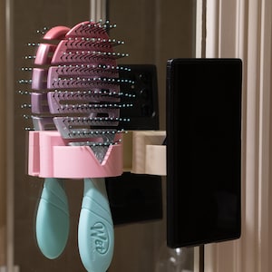 May include: A pink and purple hairbrush with a teal handle is mounted on a wall. The brush is made of plastic and has multiple rows of bristles. The handle has the word "Wet" printed on it.