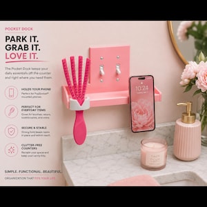 Pode incluir: Uma prateleira de parede rosa projetada para encaixar sobre um interruptor de luz duplo, com um suporte branco para uma escova de cabelo e uma ranhura para um smartphone. A prateleira é retangular com uma superfície plana e borda elevada.