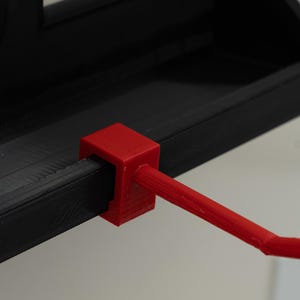 May include: A black shelf with a red support arm. The shelf has a built-in electrical outlet. The red arm is attached to the shelf and extends outward, with a curved end.