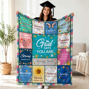 May include: A colorful blanket with inspirational text and floral designs. The blanket features squares with phrases like "Created," "Precious," and "God Says You Are." The blanket is held up by a person.