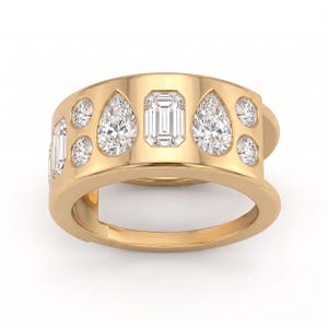 May include: A wide gold band ring featuring a central emerald-cut diamond flanked by two pear-shaped diamonds, with four smaller round brilliant-cut diamonds set into the polished gold surface on either side of the larger stones.