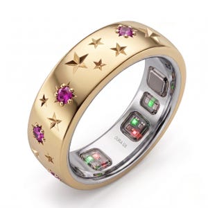 May include: A gold-toned smart ring featuring a polished exterior surface engraved with multiple star shapes and set with several small, round, vibrant pink gemstones. The interior band is silver-toned with visible electronic sensors and the text OURA G5.
