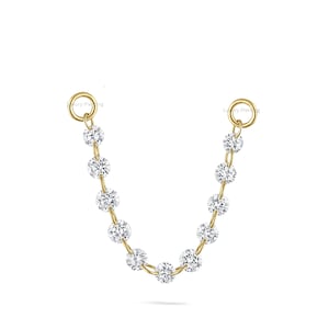 May include: A delicate gold-toned chain with sparkling, round, clear gemstones. The chain connects two small hoops, with the gemstones evenly spaced along the chain. The jewelry is set against a clean white background.
