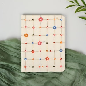 May include: A cream-colored notebook with a floral pattern. The design features colorful flowers in red, pink, orange, and blue, connected by thin brown lines. The notebook is rectangular with rounded corners.