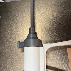 Op de afbeelding: Een witte en blauwe fles met een grijze tuit en een lange, grijze, cilindrische verlenging. De fles heeft een blauw rechthoekig etiket. De tuit heeft een schroefdraadbasis en een kleine, cilindrische knop aan de zijkant.