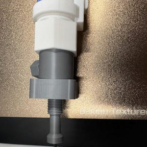 Op de afbeelding: Een 3D-geprint object in blauw, wit en grijs. Het heeft een cilindrisch ontwerp met een schroefdraad aan de onderkant en een fijne punt. Het object lijkt een mechanisch onderdeel te zijn, mogelijk voor een machine.