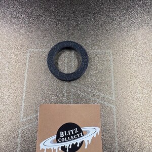 May include: A dark gray, circular object with a hole in the center. The object is textured and appears to be made of a rubber-like material. A small, square, brown card with the text "BLITZ COLLECTZ" and a planet graphic is also visible.