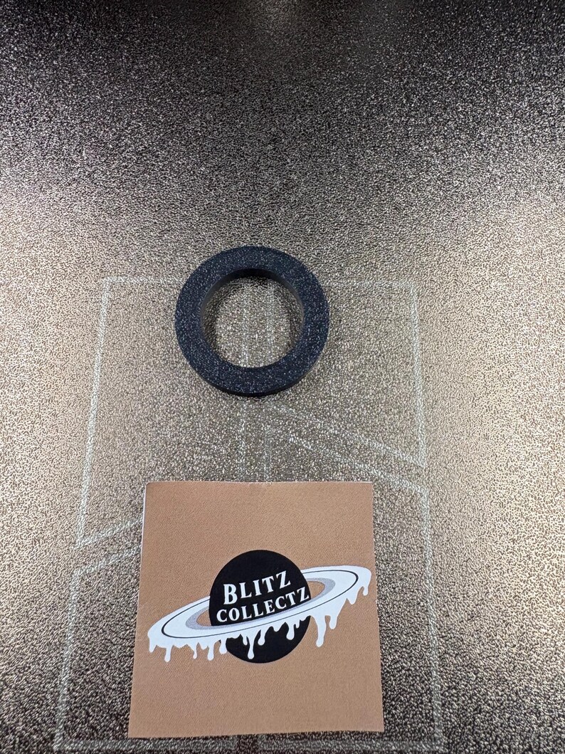 May include: A dark gray, circular object with a hole in the center. The object is textured and appears to be made of a rubber-like material. A small, square, brown card with the text "BLITZ COLLECTZ" and a planet graphic is also visible.
