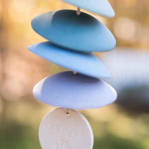 Może przedstawiać: Biały ceramiczny wiatraczek z odciskiem łapy i napisem "Harper" na okrągłej etykiecie. Wiatraczek ma pięć niebieskich ceramicznych dysk&oacute;w, kt&oacute;re wiszą.