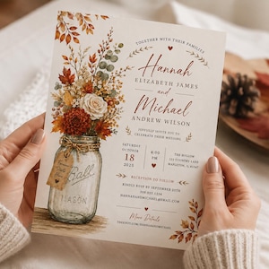 May include: A wedding invitation card featuring a watercolor illustration of a mason jar filled with autumn flowers and foliage. The text includes the names Hannah Elizabeth James and Michael Andrew Wilson, the date October 18, 2025, and venue details.
