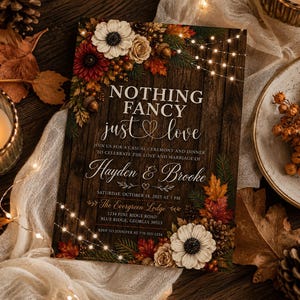 May include: A rectangular wedding invitation card with a dark wood grain background, decorated with autumn leaves, pinecones, and white flowers. The text reads: NOTHING FANCY just love, Hayden & Brooke, Saturday, October 18, 2025 at 5 PM.