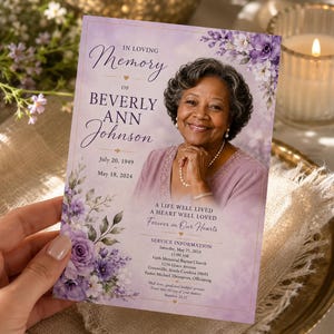 May include: A rectangular funeral program card featuring a portrait of a smiling person, purple floral illustrations, and the text: In Loving Memory of Beverly Ann Johnson, July 20, 1949 - May 18, 2024, A Life Well Lived, A Heart Well Loved, Forever in Our Hearts.