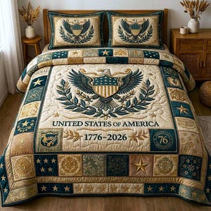 Könnte beinhalten: Cremefarbenes Steppdecken-Set mit amerikanischem Adler-Emblem, dem Text „UNITED STATES OF AMERICA 1776-2026“ und dekorativen Quadraten. Enthält zwei passende Kissenbezüge. Die Steppdecke hat einen marineblauen und goldenen Rand mit Sternakzenten.