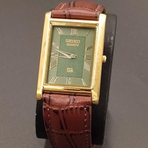 May include: A rectangular gold-toned Seiko Quartz watch with a green face and brown leather band. The watch face features Roman numerals and the Seiko logo. The band has a crocodile pattern.