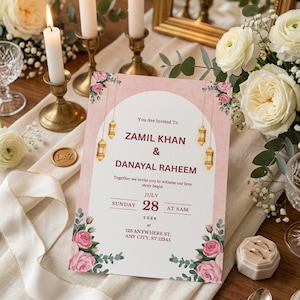 Puede incluir: Una tarjeta de invitaci&oacute;n de boda rectangular con un dise&ntilde;o de arco rosa y blanco, linternas doradas colgantes e ilustraciones de rosas rosas. El texto dice: You Are Invited To ZAMIL KHAN & DANAYAL RAHEEM, JULY SUNDAY 28 AT 8AM 2026, 123 ANYWHERE ST, ANY CITY, ST 12345.
