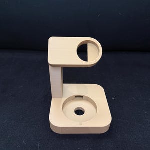 Puede incluir: Un soporte beige impreso en 3D con una parte superior e inferior circulares, conectado por un soporte vertical. La parte superior presenta un recorte semicircular, y la base tiene una hendidura circular central. El soporte est&aacute; dise&ntilde;ado para sostener un art&iacute;culo.