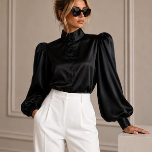 May include: A black satin long-sleeve blouse featuring a high collar, a front button placket, and voluminous puff sleeves with fitted cuffs, paired with high-waisted white trousers that have a clean, tailored front pleat design.