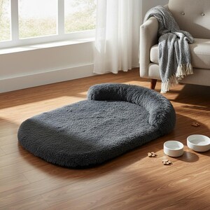May include: A rectangular dark gray pet bed with a plush, shaggy texture and a raised bolster along one end. The bed is accompanied by two plain white ceramic bowls and several small wooden paw-shaped decorative accents on the floor.