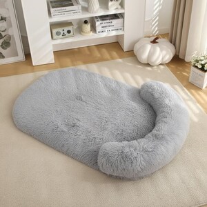 May include: A rectangular light gray pet bed featuring a plush, shaggy faux fur texture. The bed has a raised, curved bolster along one side, providing a cushioned edge while the rest of the surface remains flat and soft for resting.