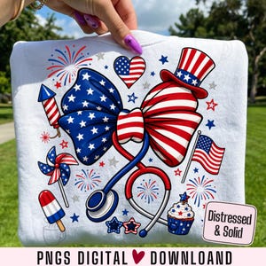 May include: White sweatshirt featuring a patriotic design with a large bow in red, white, and blue, a stethoscope, and various American flag-themed elements. Includes fireworks, stars, a cupcake, and the text "PNGS DIGITAL DOWNLOAD".