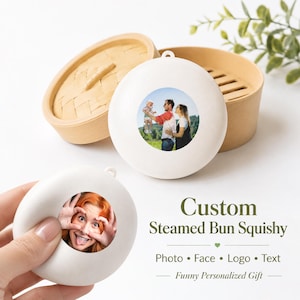 May include: Two white round squishy toys shaped like steamed buns, each featuring a circular photo print on the front. One toy shows a family outdoors, while the other shows a person making a face. A bamboo steamer basket is in the background.