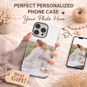 Puede incluir: Una funda de teléfono personalizada blanca con la foto de una pareja, sostenida por una persona. La funda tiene un recorte negro para la lente de la cámara. La imagen también incluye un teléfono que muestra la misma foto y el texto "Perfect Personalized Phone Case" y "Your Photo Here".