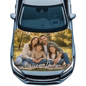 Puede incluir: Capó de coche azul con una foto familiar y el texto "Custom Design" en cursiva. La imagen muestra a una familia sonriente de cuatro personas sentadas en una manta en un campo con árboles al fondo.