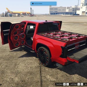May include: A custom red pickup truck with multiple speakers installed in the doors and truck bed. The truck has black rims and a lowered suspension. The doors are open, revealing the speaker configuration.