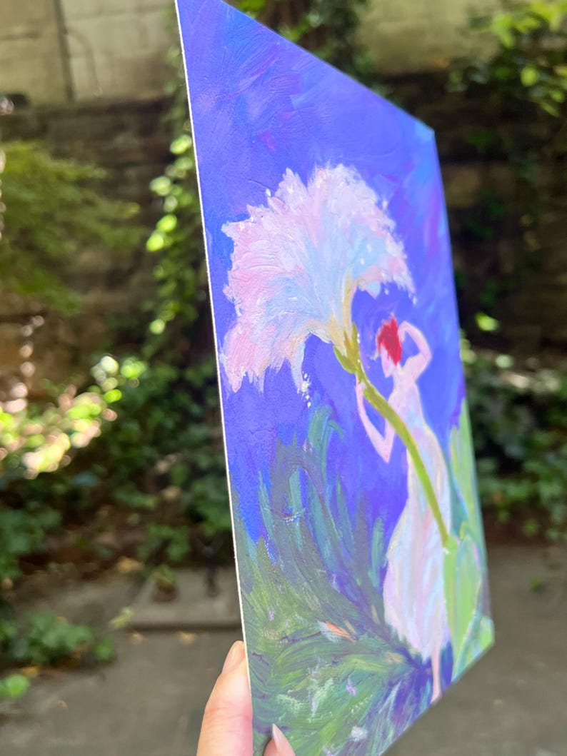 Puede incluir: Pintura original sobre lienzo que representa una figura que se extiende hacia una gran flor blanca y rosa sobre un fondo azul. La obra de arte presenta a una mujer con un vestido blanco y cabello rojo, rodeada de follaje verde. La pintura se sostiene en &aacute;ngulo.