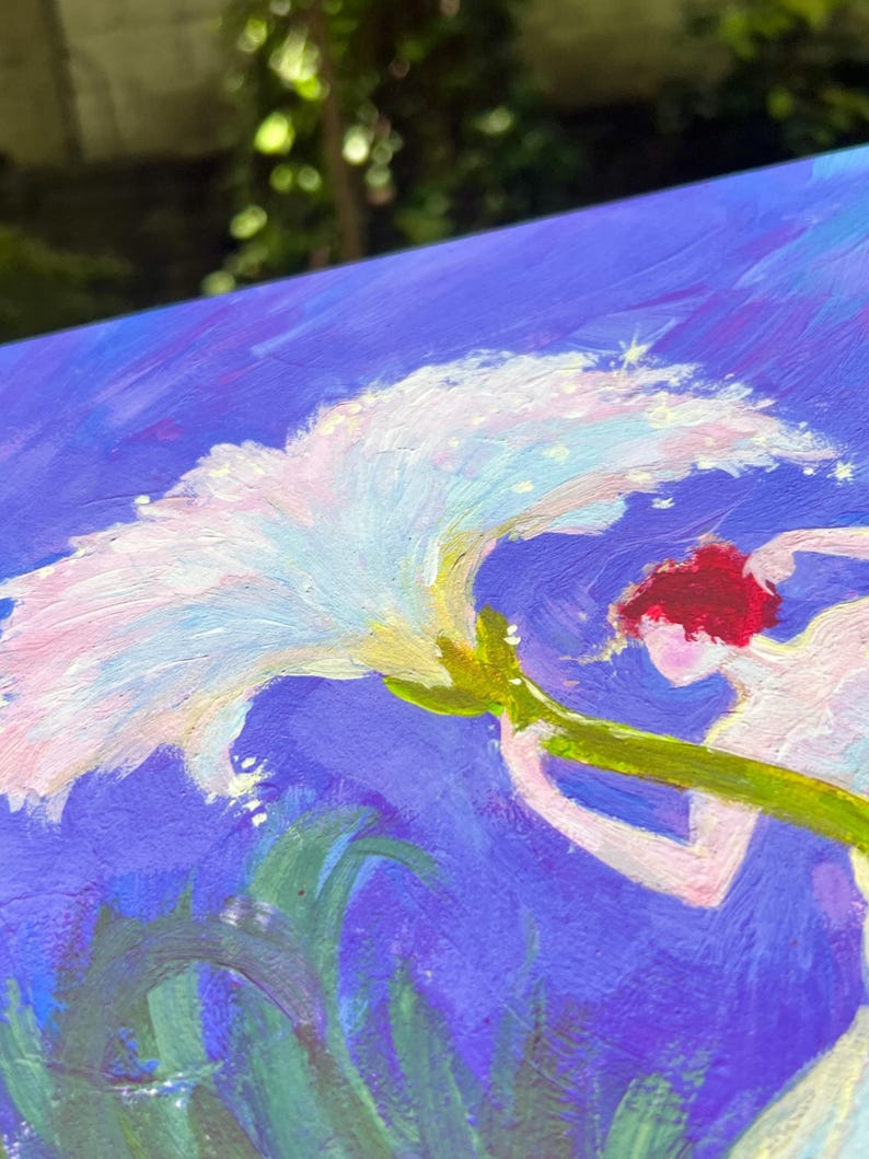 Puede incluir: Pintura impresionista que presenta una flor blanca con acentos rosas y amarillos, sostenida por una figura con cabello rojo. El fondo es azul vibrante con pinceladas verdes y azules que sugieren follaje. La obra tiene una cualidad on&iacute;rica y et&eacute;rea.