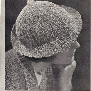 May include: A close-up of a woman wearing a crocheted hat. The hat is a light gray color and has a wide brim. The woman is looking down and her face is partially obscured by the hat.