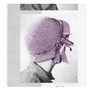 May include: A purple crocheted cloche hat with a matching ribbon tied in a bow. The ribbon has the word "Stitches" printed on it.