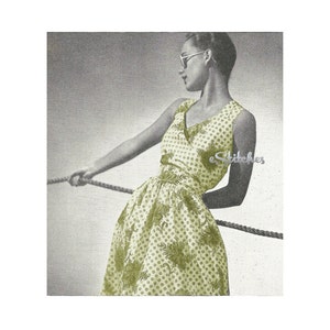 May include: A woman wearing a sleeveless dress with a green and white floral pattern. The dress has a V-neckline and a fitted bodice. The woman is holding a rope in her hands and is looking to the side.