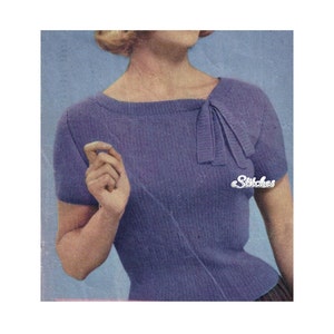 Puede incluir: Un suéter de punto morado con un detalle de lazo en el escote. El suéter tiene mangas cortas y una silueta ajustada.