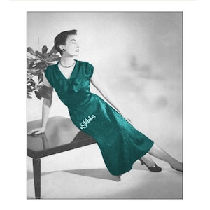 May include: A teal green dress with a V-neck and a bow at the neckline. The dress is fitted and has a skirt that falls to the knees. The model is wearing the dress and is posing with her hand on a table.